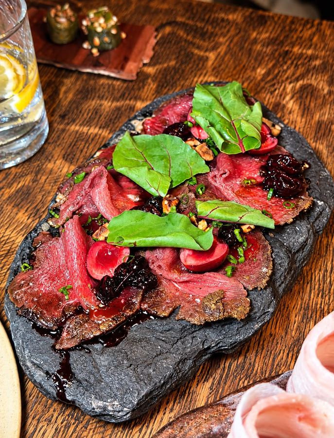 Carpaccio mit Kirschen und Haselnuss auf einer Steinplatte